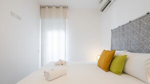 Un lit bien fait, avec un matelas blanc, une serviette enroulée et deux oreillers (un jaune et un vert).
