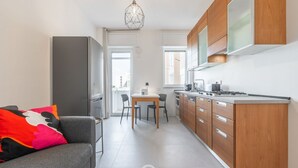 Une cuisine compacte avec des meubles en bois, un coin repas avec une table et des chaises, et un canapé gris agrémenté d’un coussin coloré.
