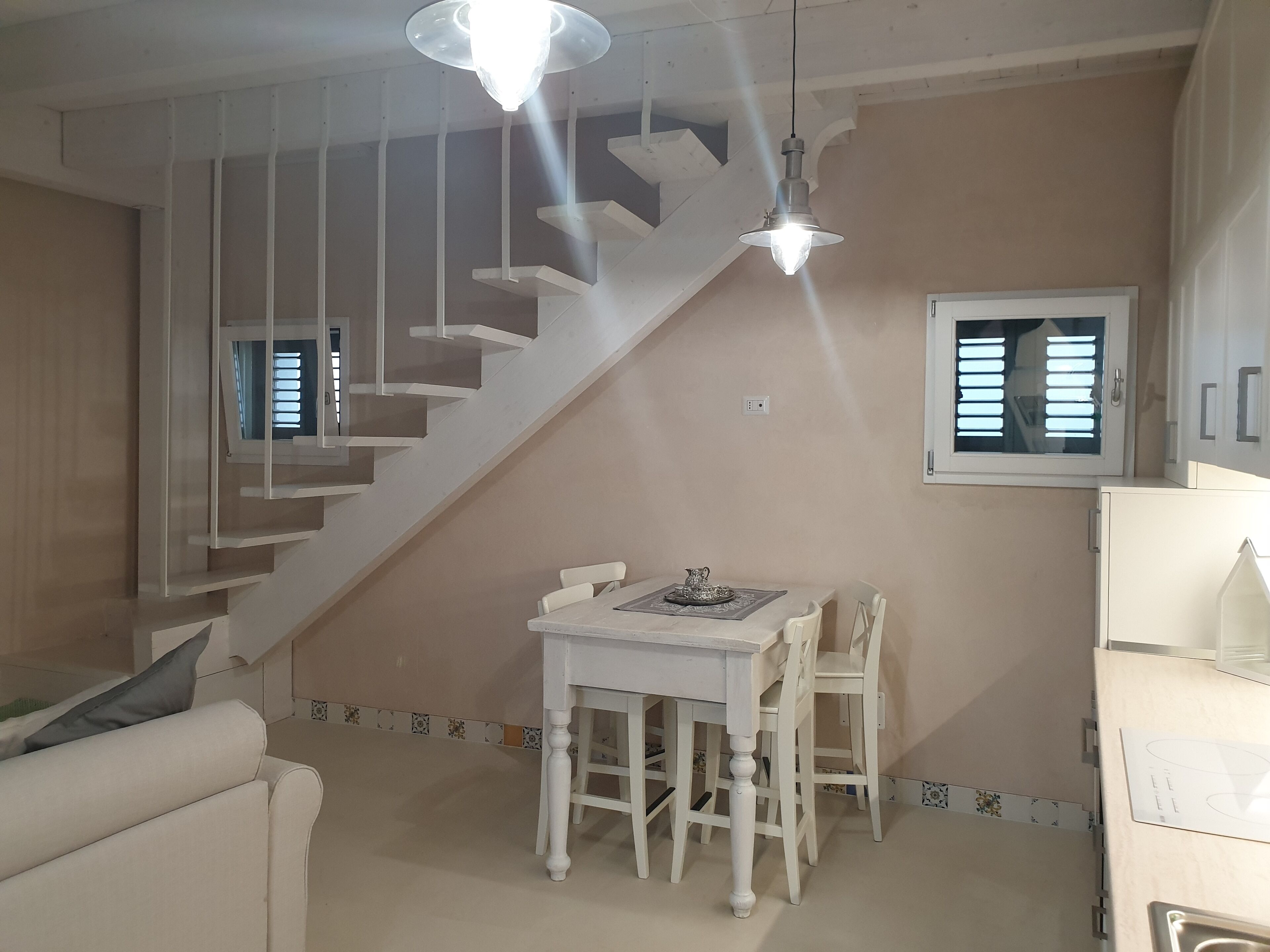A modern interior with a staircase, a dining area with a table and chairs, and a kitchen area with a refrigerator.