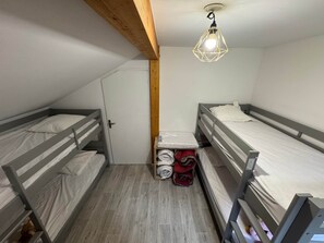 Ein Schlafsaalzimmer mit Etagenbetten, einem Holzbalken an der Decke, einer kleinen Ablage mit gefalteten Decken und einer Hängelampe.