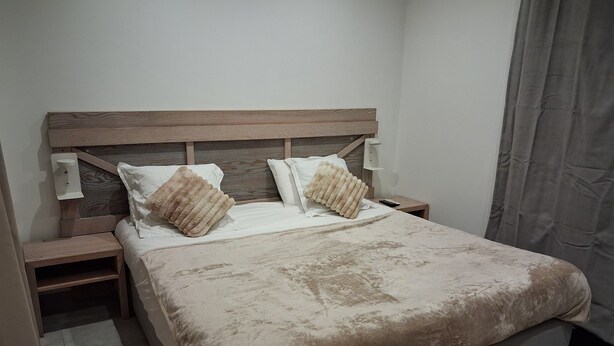A bedroom with a bed, two bedside tables, a nightstand, a blanket, and a pillow.