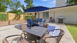 Een terras buiten met een tafel, stoelen, een blauwe parasol en een barbecue.