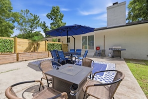 An outdoor patio with a table and chairs, a blue umbrella, and a grill. - One Love | 3BR Home · Fenced Yard · Near I-95 (Smithfield)