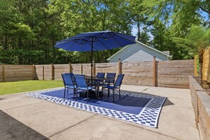An outdoor patio with a table and chairs, a blue umbrella, and a patterned rug. - Pet-Friendly 3BR | Fenced Yard (Smithfield)