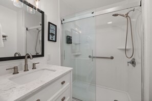 A modern bathroom with a glass shower enclosure, a marble sink, and a large mirror. - One Love | 3BR Home · Fenced Yard · Near I-95 (Smithfield)