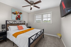 A bedroom with a bed, a ceiling fan, a painting, a TV, a window, and a nightstand. - Pet-Friendly 3BR | Fenced Yard (Smithfield)