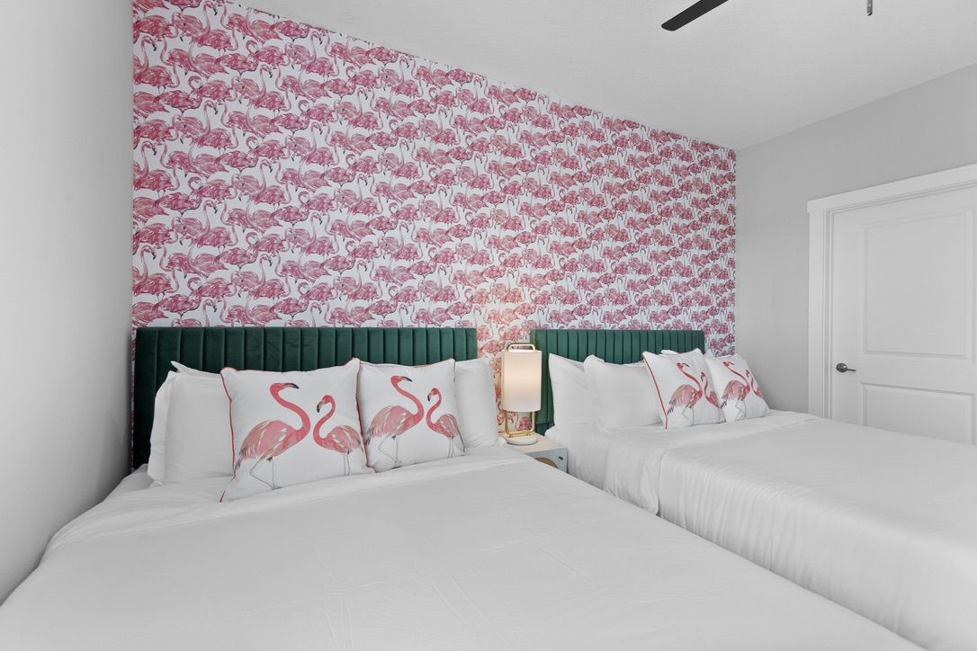 A double bed with white bedding and pillows featuring flamingo designs, a bedside lamp, and a wall with a flamingo pattern.
