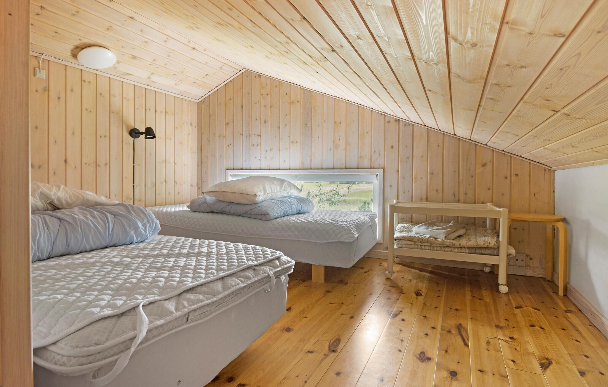 Une chambre confortable située dans les combles, avec des murs en bois et un plafond en pente, comprenant deux lits et une petite table.