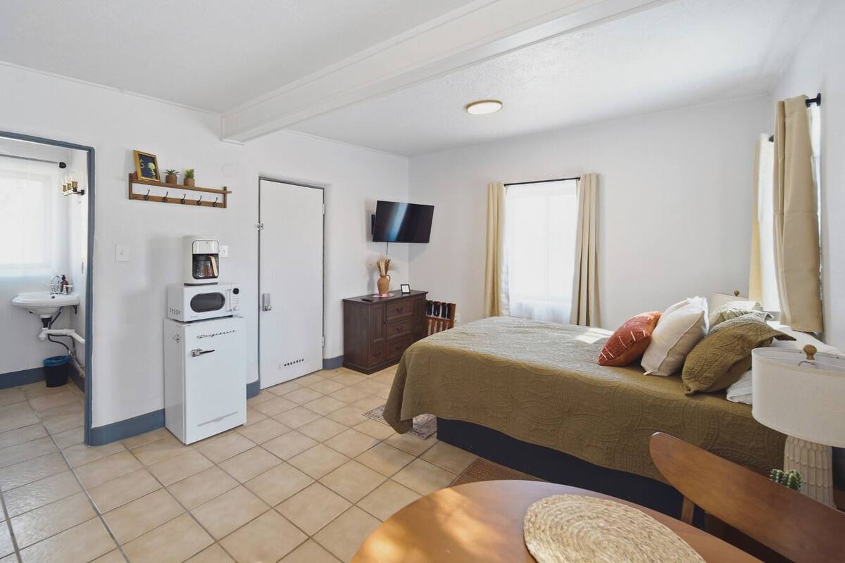 A hotel room with a bed, a TV, a coffee maker, a dresser, and a window with curtains.