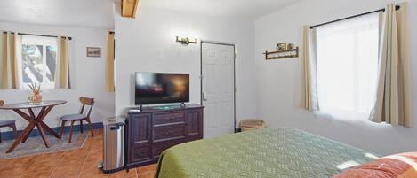 Une chambre d’hôtel comprenant un lit, un bureau avec une chaise, une télévision, une armoire et une fenêtre avec des rideaux.