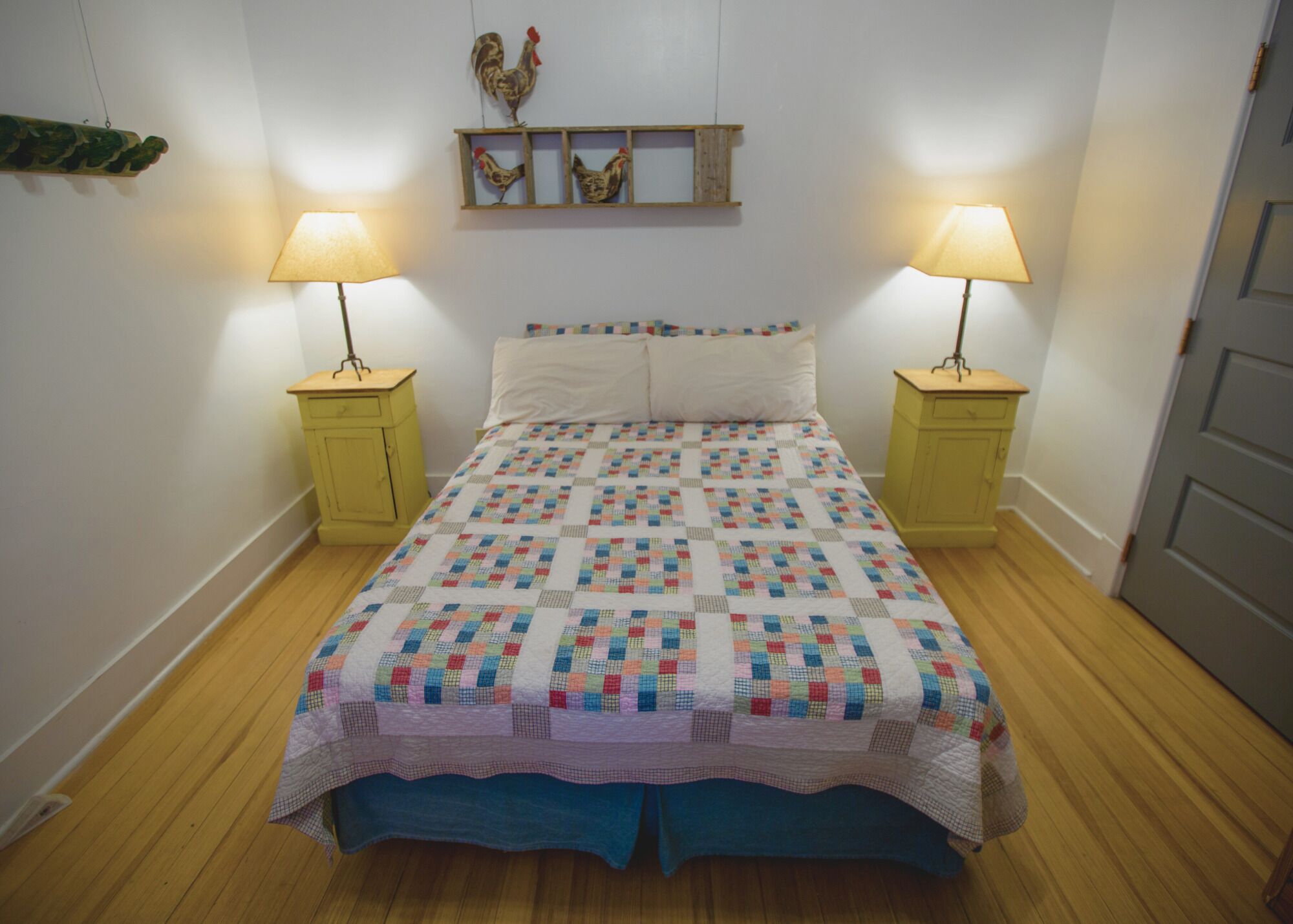 Ein Schlafzimmer mit gesteppter Bettdecke, zwei Nachttischlampen, einem Holzregal mit Dekoration und einer Tür.