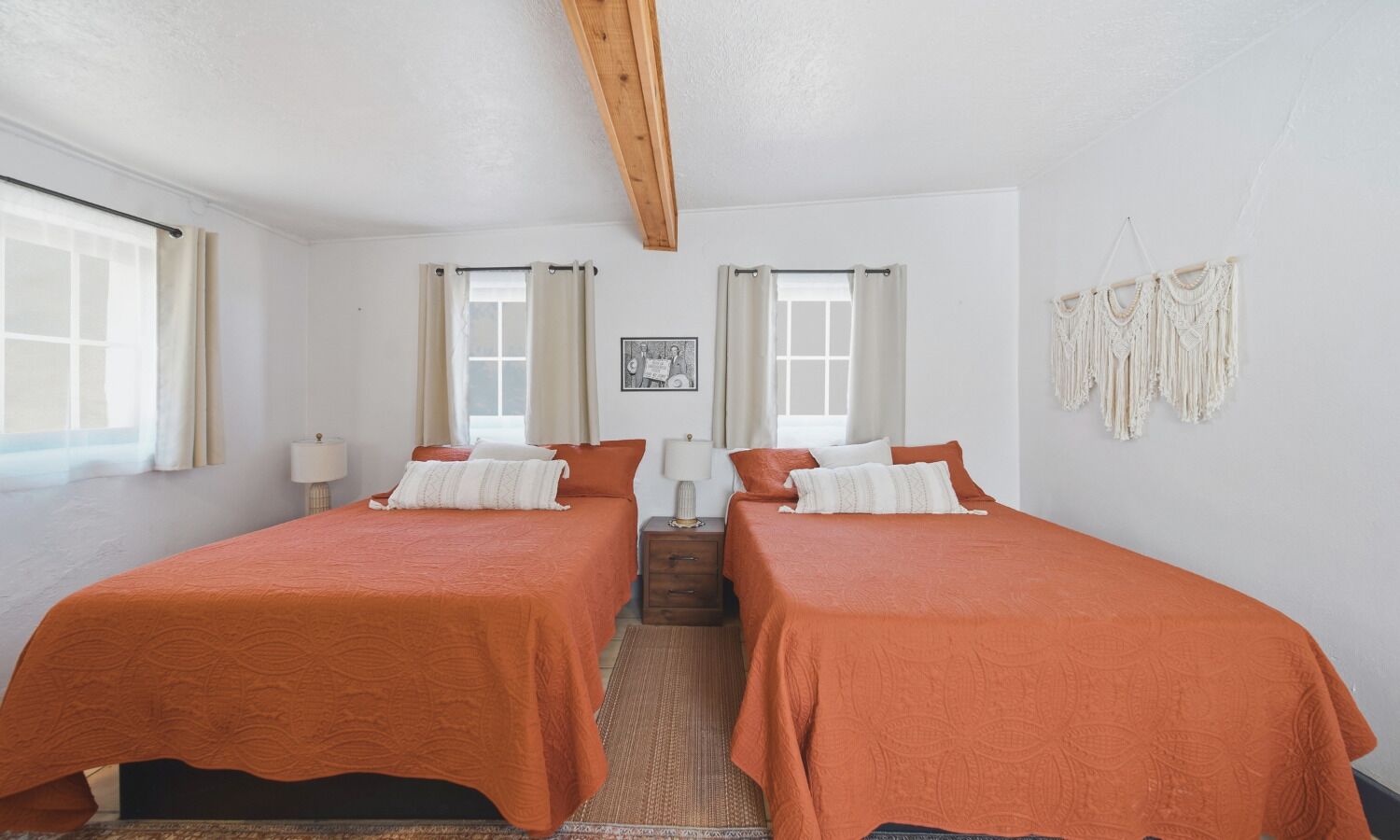 A bedroom with two beds, a wooden ceiling, a small table, and a macrame wall hanging.