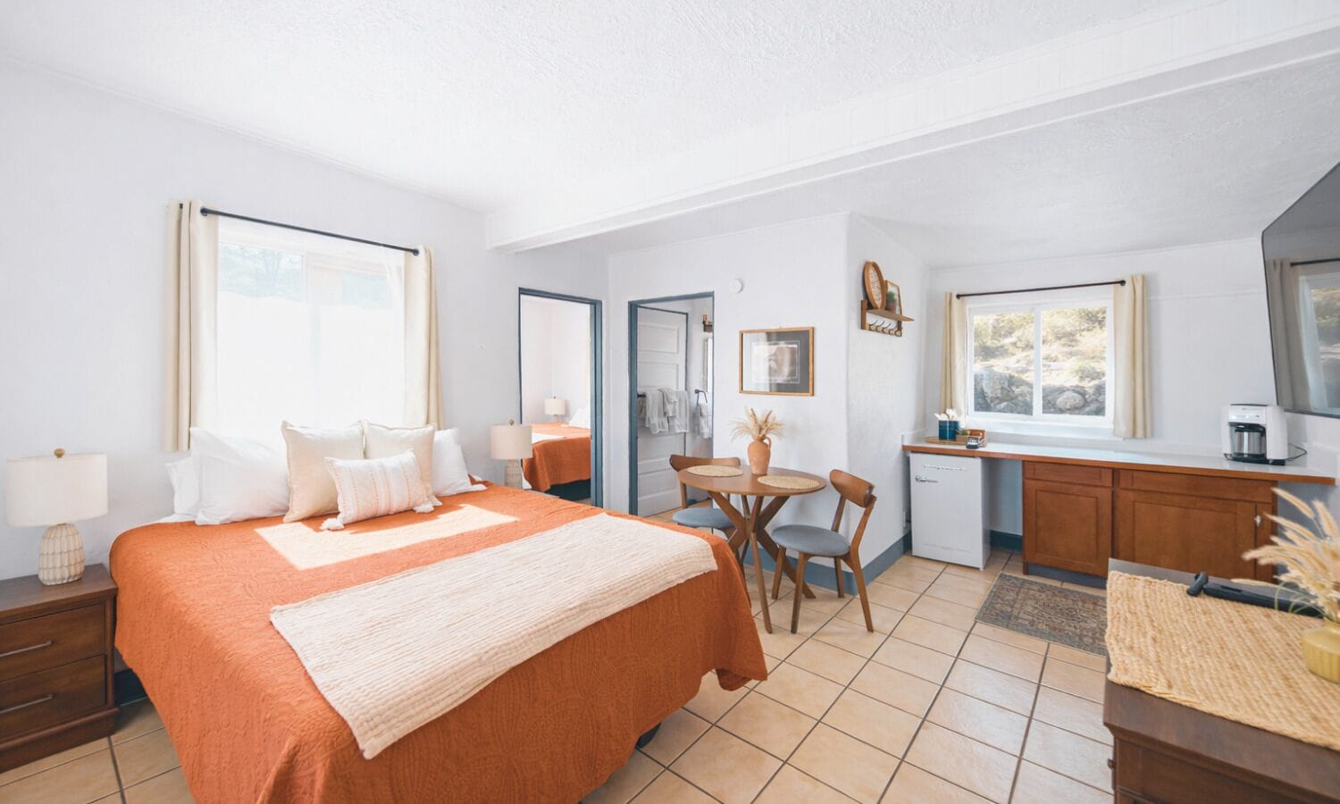 A hotel room with a large bed, a small dining table, a kitchenette, and a bathroom.