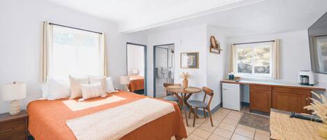 A hotel room with a large bed, a small dining table, a kitchenette, and a bathroom.