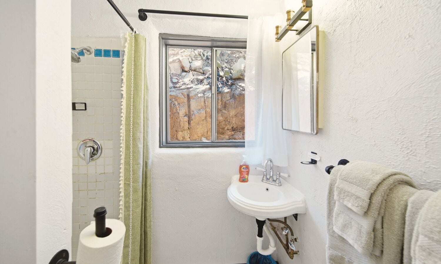 A bathroom with a shower, a sink, a window with a view of rocks, and a towel rack.