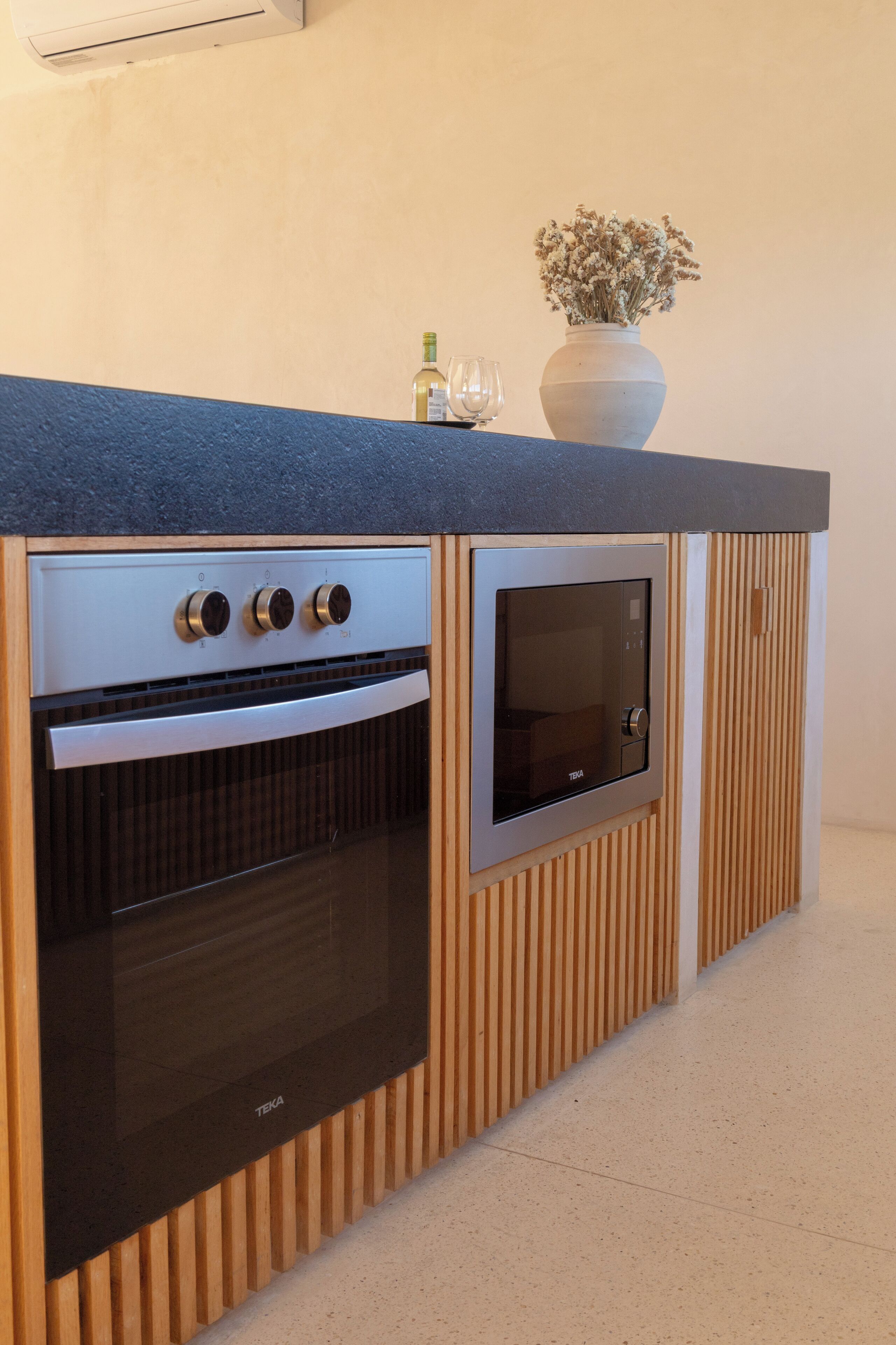 A modern kitchen with a built-in oven and microwave, wooden paneling, and a vase with dried flowers on the countertop.