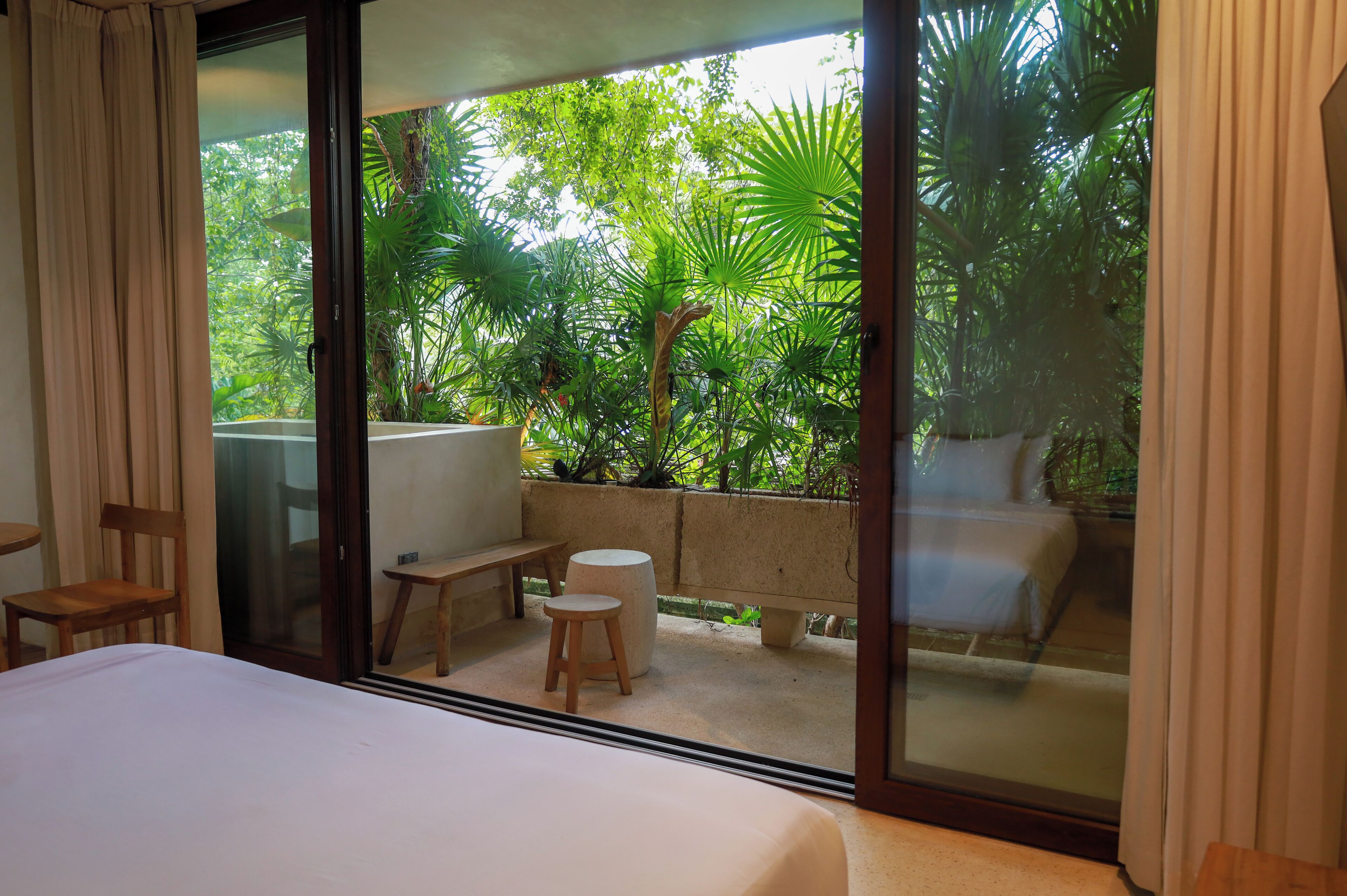 A bedroom with a large sliding glass door leading to a balcony with a view of lush greenery.
