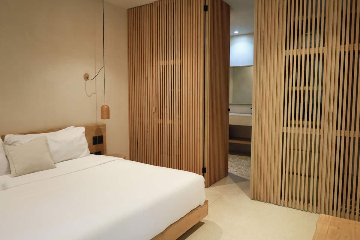 A modern hotel room with a wooden bed frame, a large window, and a wooden partition.
