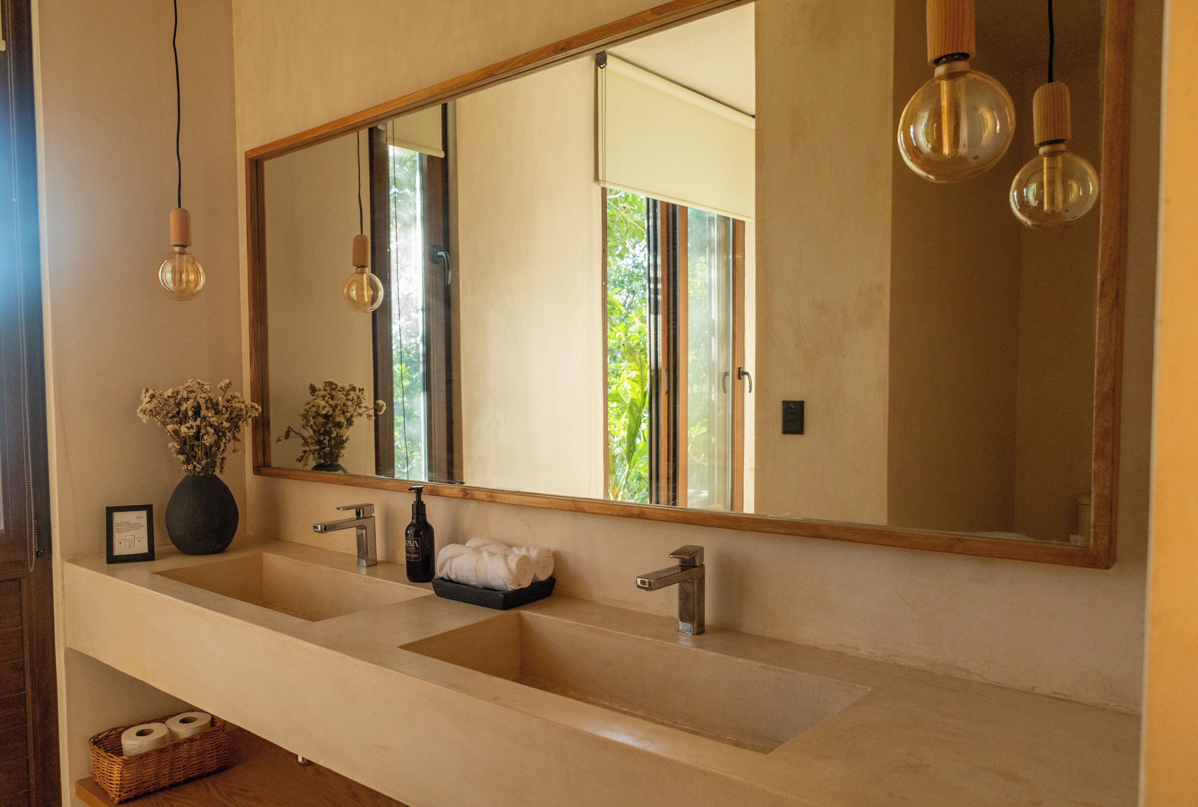 A bathroom with a large mirror, two sinks, a towel rack, and a vase of flowers.