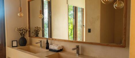 A bathroom with a large mirror, two sinks, a towel rack, and a vase of flowers.