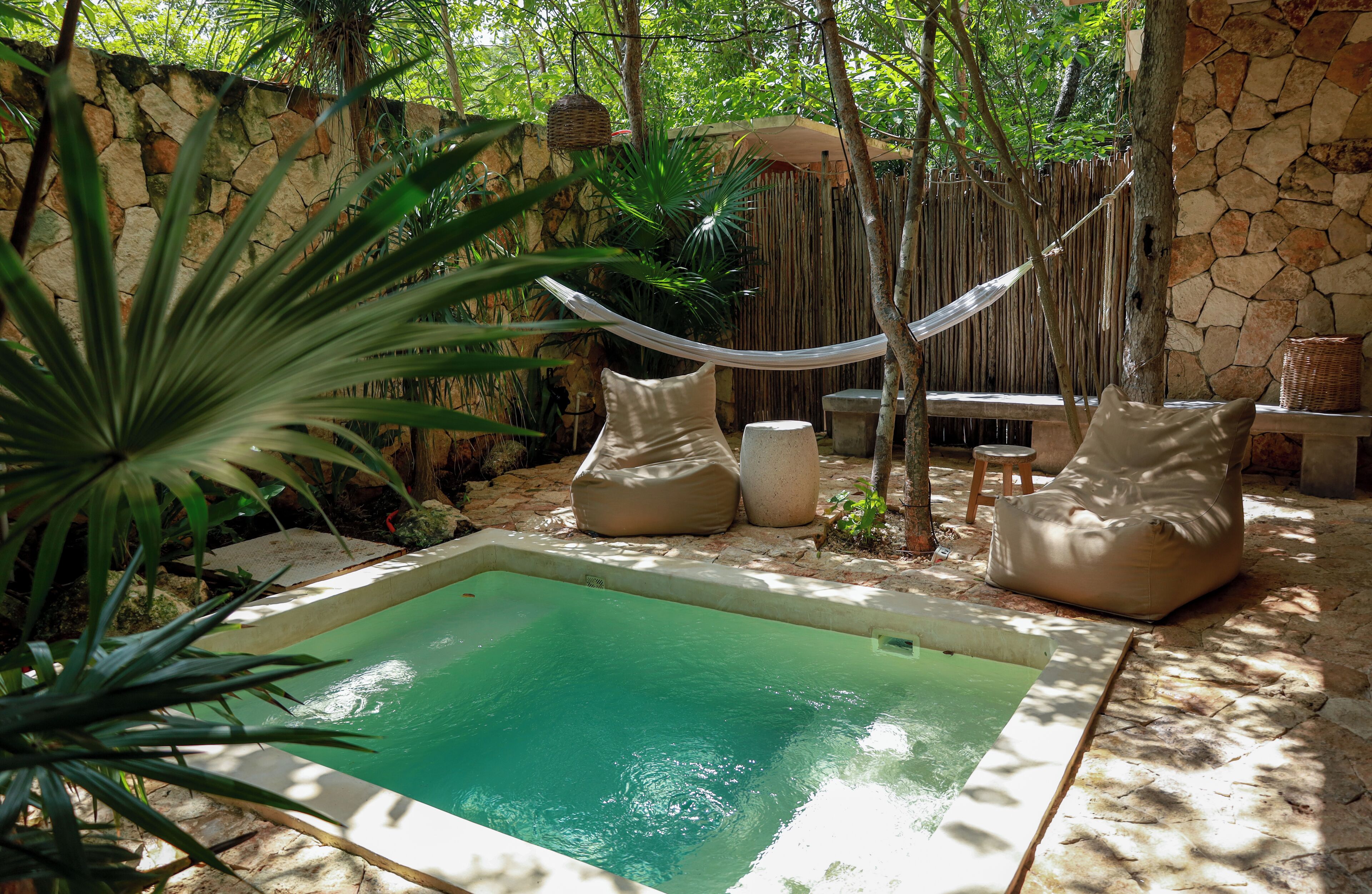 A small outdoor pool area with a stone wall, a hammock, and seating.