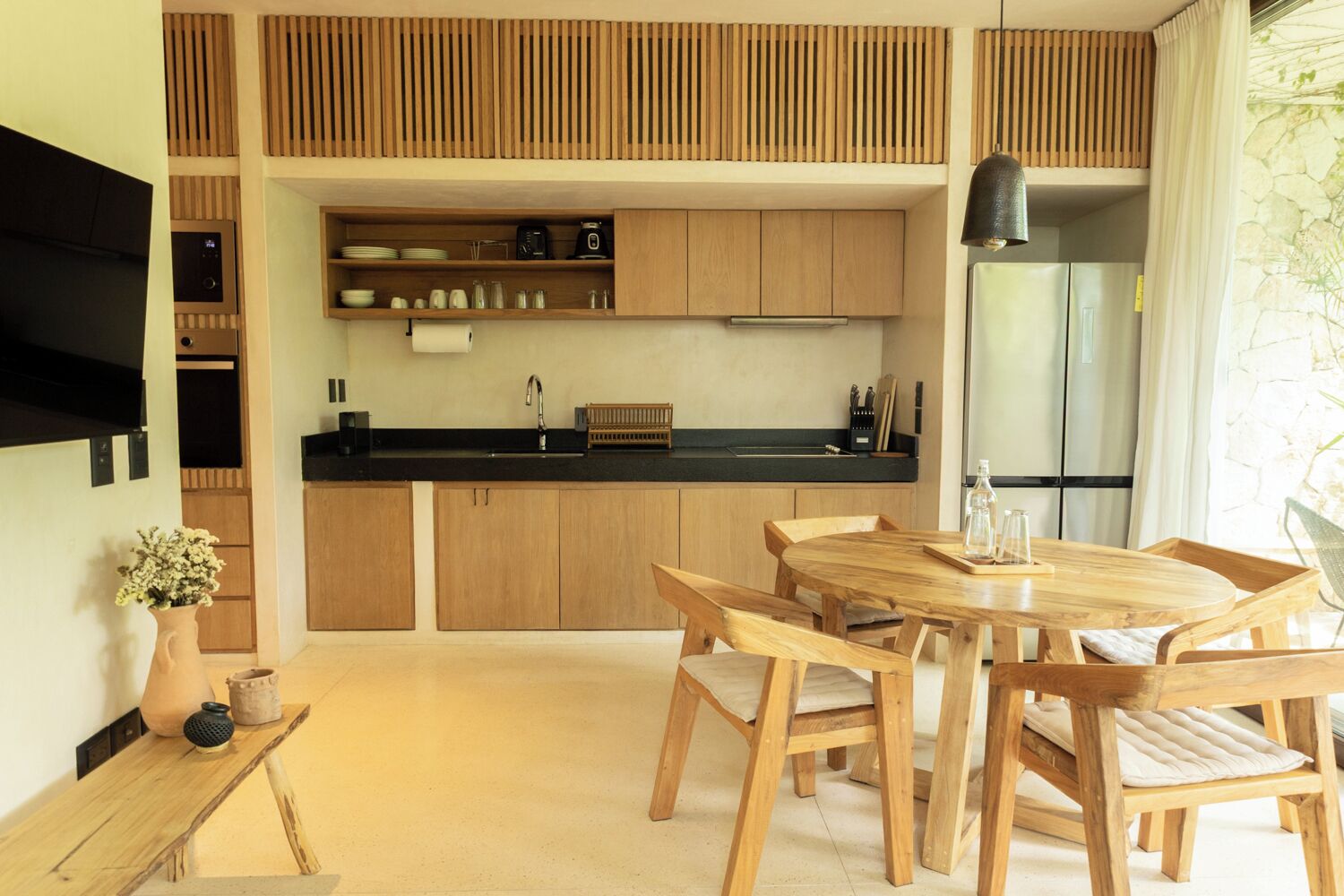 A modern kitchen with wooden cabinets, a black countertop, and a dining area with a wooden table and chairs.