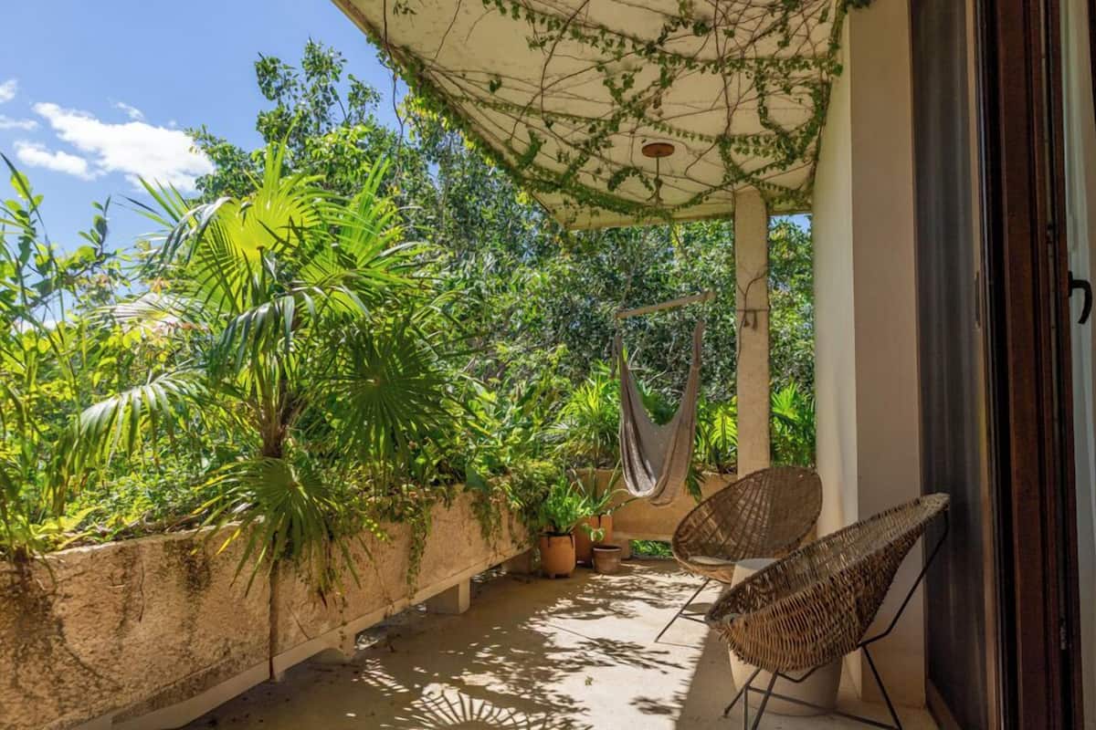 A covered outdoor area with a hammock, wicker chairs, and potted plants.