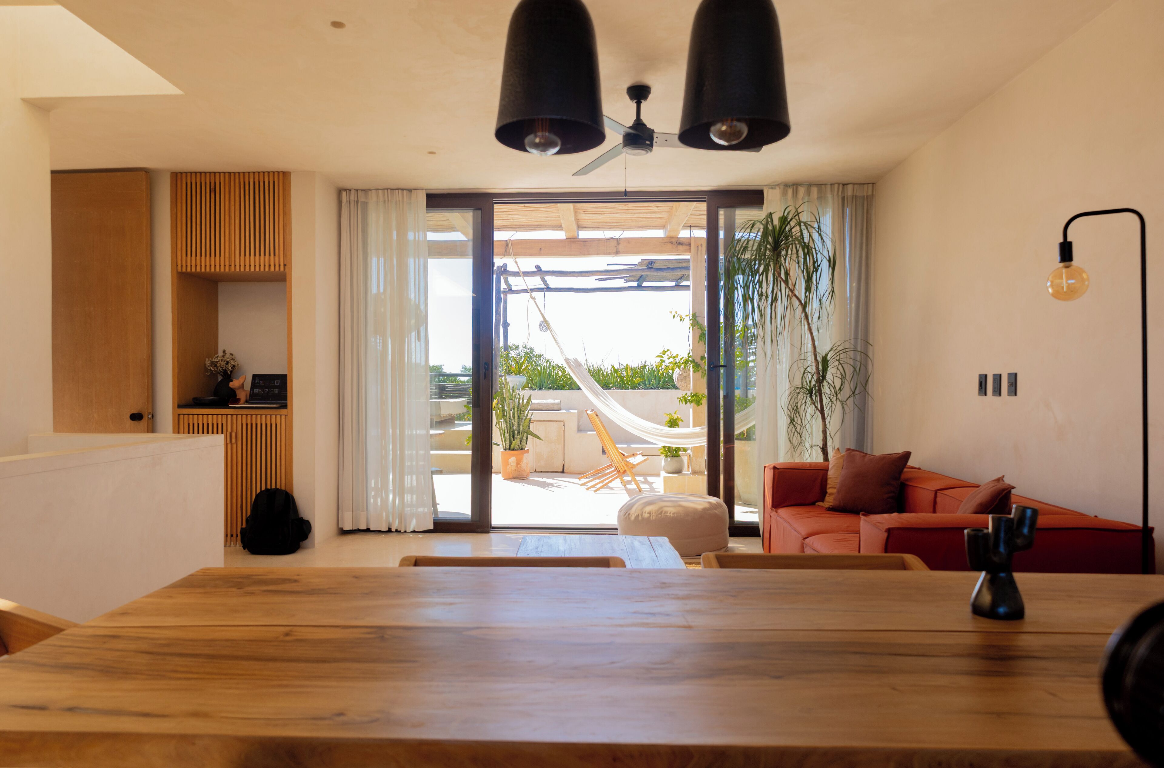 A spacious living area with a wooden dining table, a red sofa, and a hammock on a balcony.