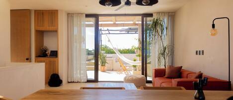 A spacious living area with a wooden dining table, a red sofa, and a hammock on a balcony.