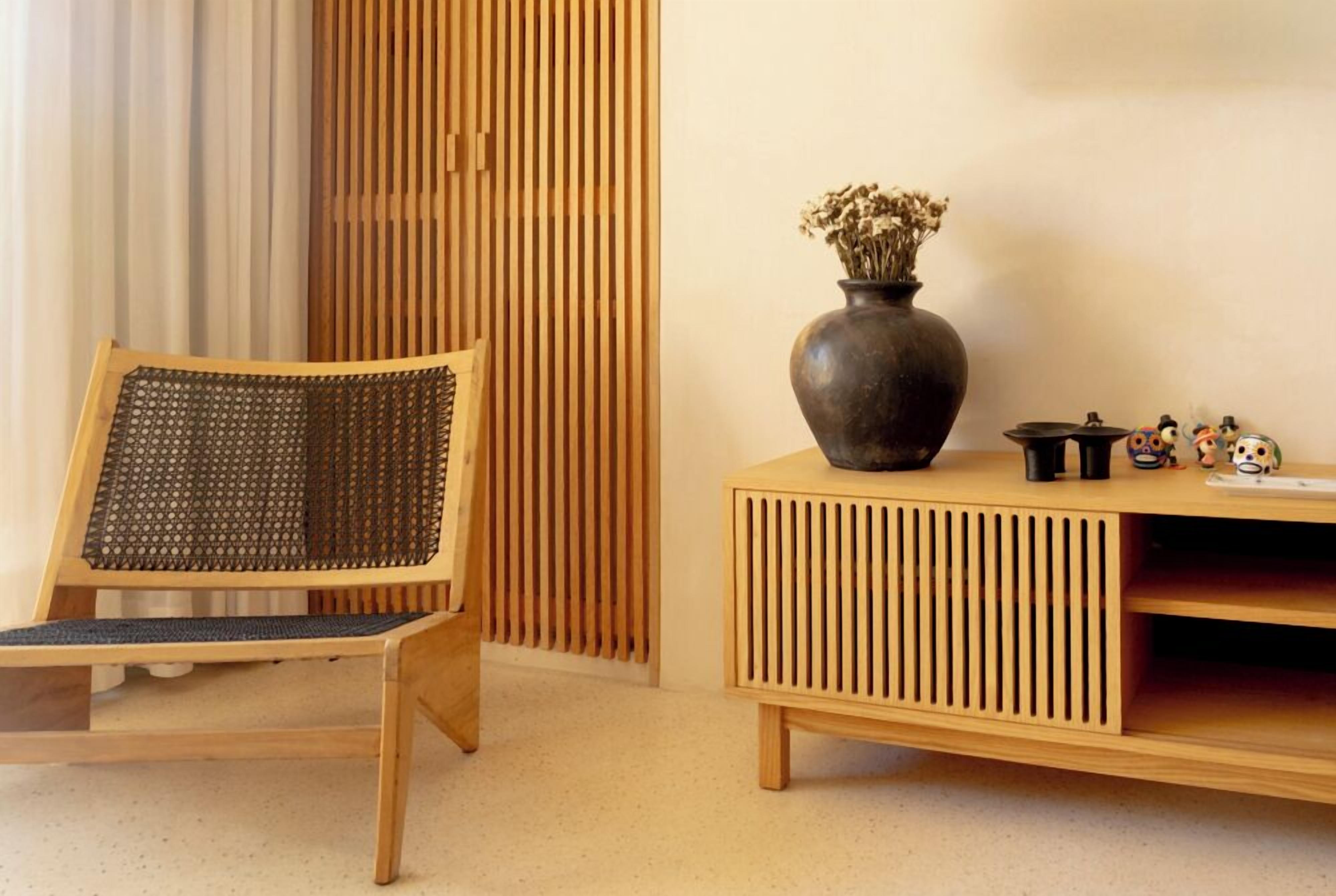 A room with a wooden chair, a dark vase with dried flowers, and a wooden console table with kitchen items.