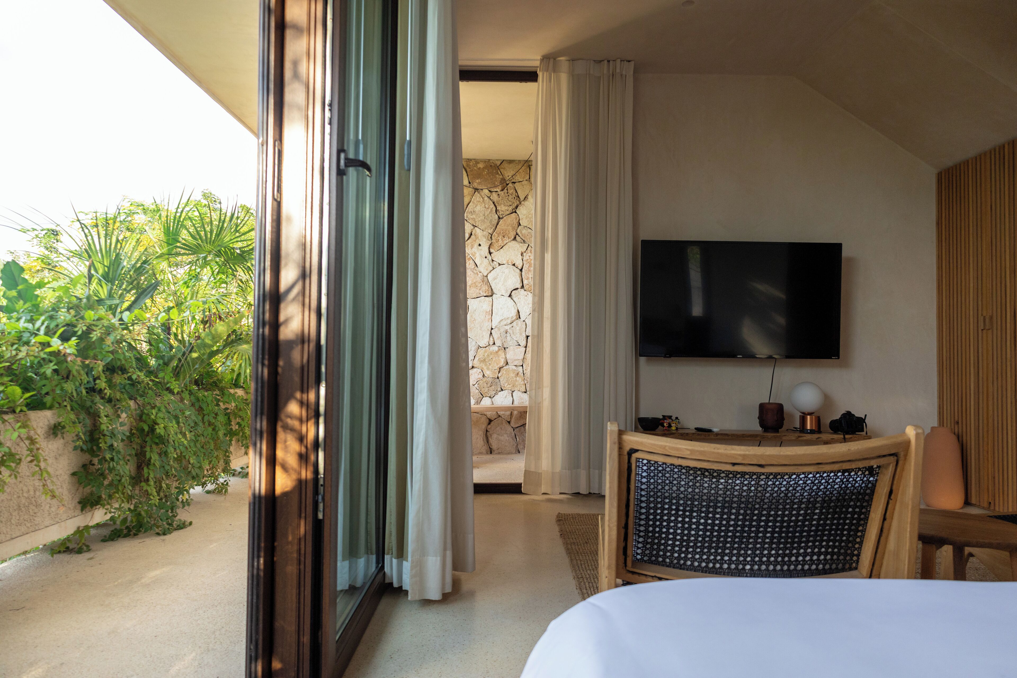 Habitación de hotel con una cama, un televisor, un escritorio con lámpara y una pared de piedra.