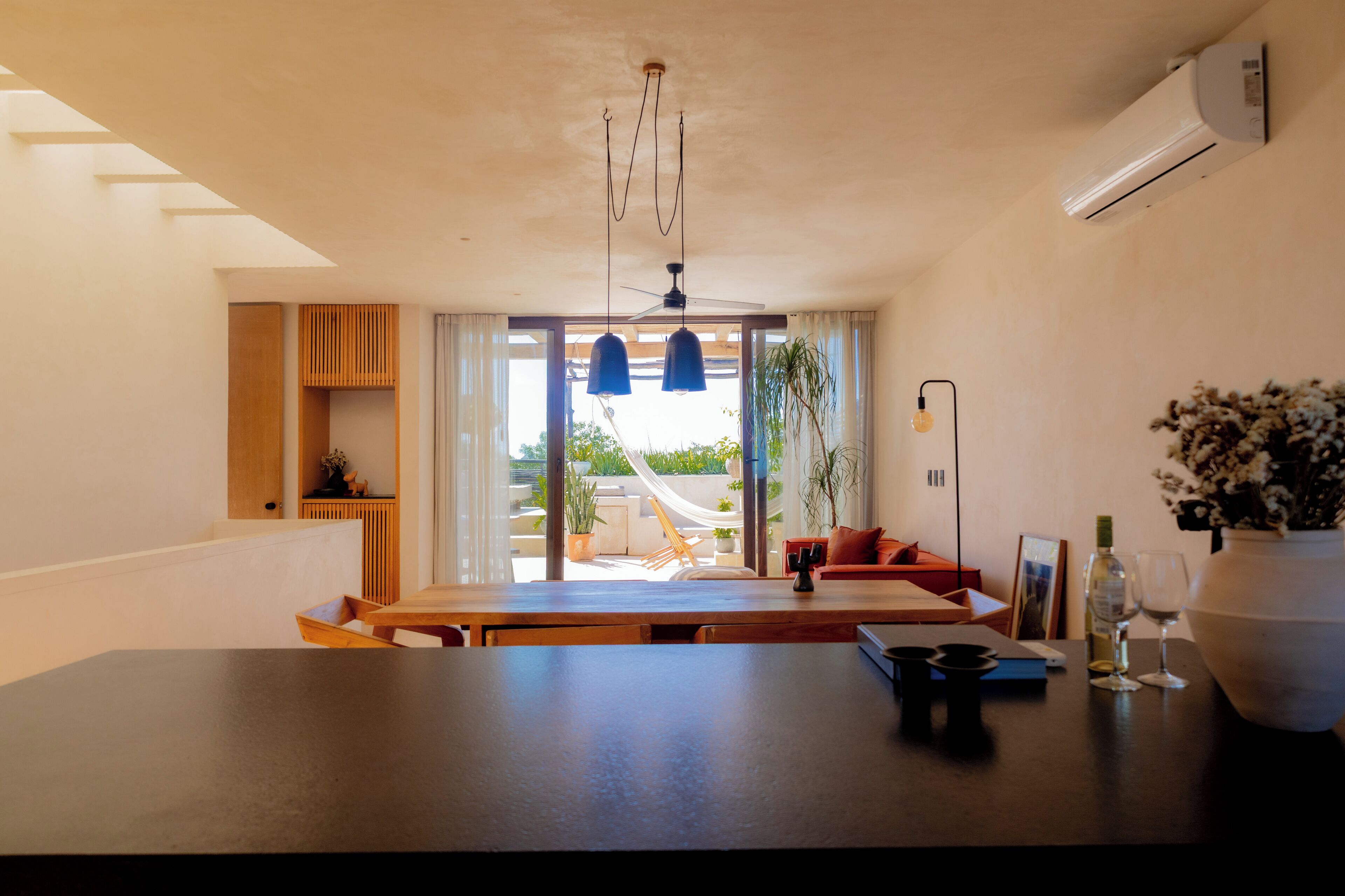 Un salon moderne avec une table en bois foncé, un canapé et une grande fenêtre donnant sur un jardin.