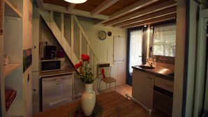 A kitchen with wooden beams, a white refrigerator, a microwave, a sink, and a vase with red flowers on the counter. - Chalet avec piscine au Domaine du Lac de Goulens (LAYRAC)