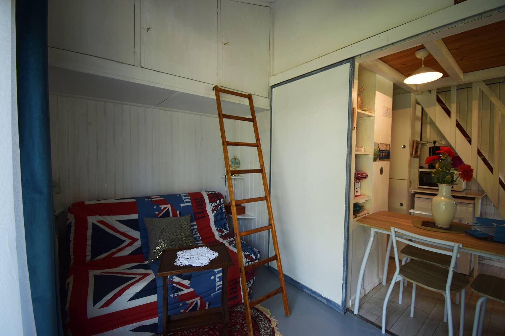 Une pièce chaleureuse avec un lit en mezzanine, une échelle en bois, une table à manger avec des chaises et un coin cuisine avec un escalier.