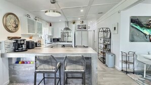 Een moderne keuken met een centraal eiland, barkrukken, een eethoek en een zithoek met een televisie en kunstwerken.