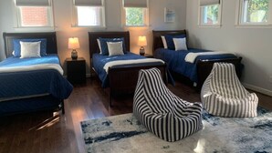 A bedroom with three beds, a striped bean bag chair, and a blue and white rug.