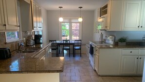 A kitchen with granite countertops, white cabinets, a dining area with a table and chairs, and pendant lighting.