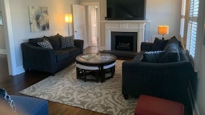 A living room with two dark sofas, a round coffee table, a fireplace, and a flat-screen TV mounted above it.