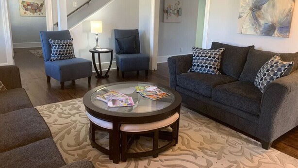 A living room with a round coffee table, two armchairs, a sofa, and a staircase in the background.