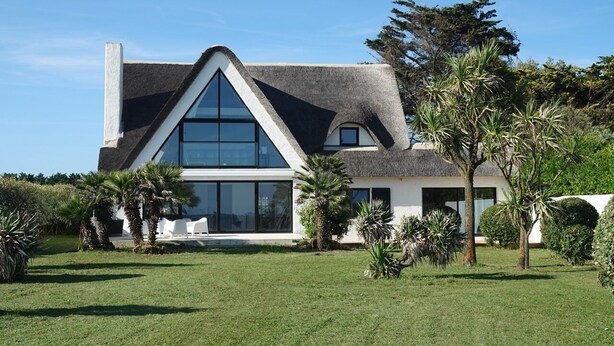A modern house with a large glass window, a sloped roof, and a well-maintained lawn. - Villa "La Loubine" contemporary thatched cottage facing the sea (Batz-sur-Mer)