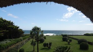 A coastal view from a thatched-roof structure with a well-maintained lawn and various shrubs. - Villa "La Loubine" contemporary thatched cottage facing the sea (Batz-sur-Mer)