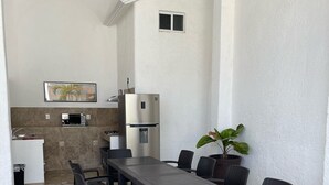 Un espacio moderno para comer al aire libre con una mesa larga y sillas, un refrigerador y un microondas.