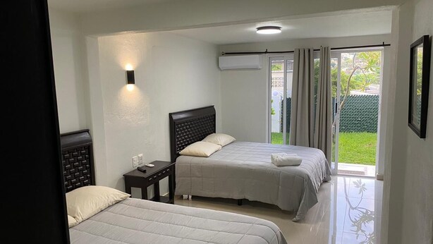 Habitación de hotel con dos camas, una mesita de noche, una lámpara fijada a la pared y un ventanal corredero a un balcón.