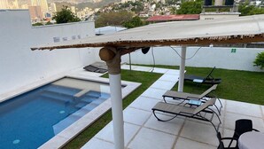 Un área de piscina en la azotea con una pérgola, sillones de descanso y una mesa.