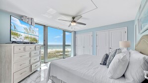 Un dormitorio con una cama grande, televisión, ventilador de techo y vista a la playa.