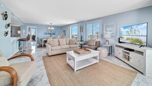 Un salón espacioso con pared azul claro, un sofá color beige, una mesa de centro blanca y un televisor sobre un mueble blanco.