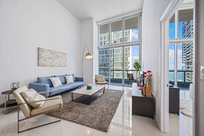 A modern living room with a blue sofa, a coffee table, and a large window offering a view of the cityscape.
