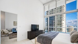 A modern bedroom with a large bed, a TV, and a view of the cityscape. - 40th Floor High Ceiling Condo-Bay View - Free Spa (Miami)