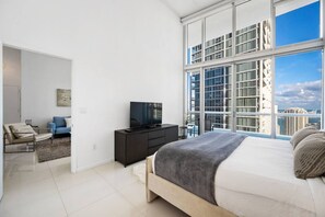 A modern bedroom with a large bed, a TV, and a view of the cityscape.