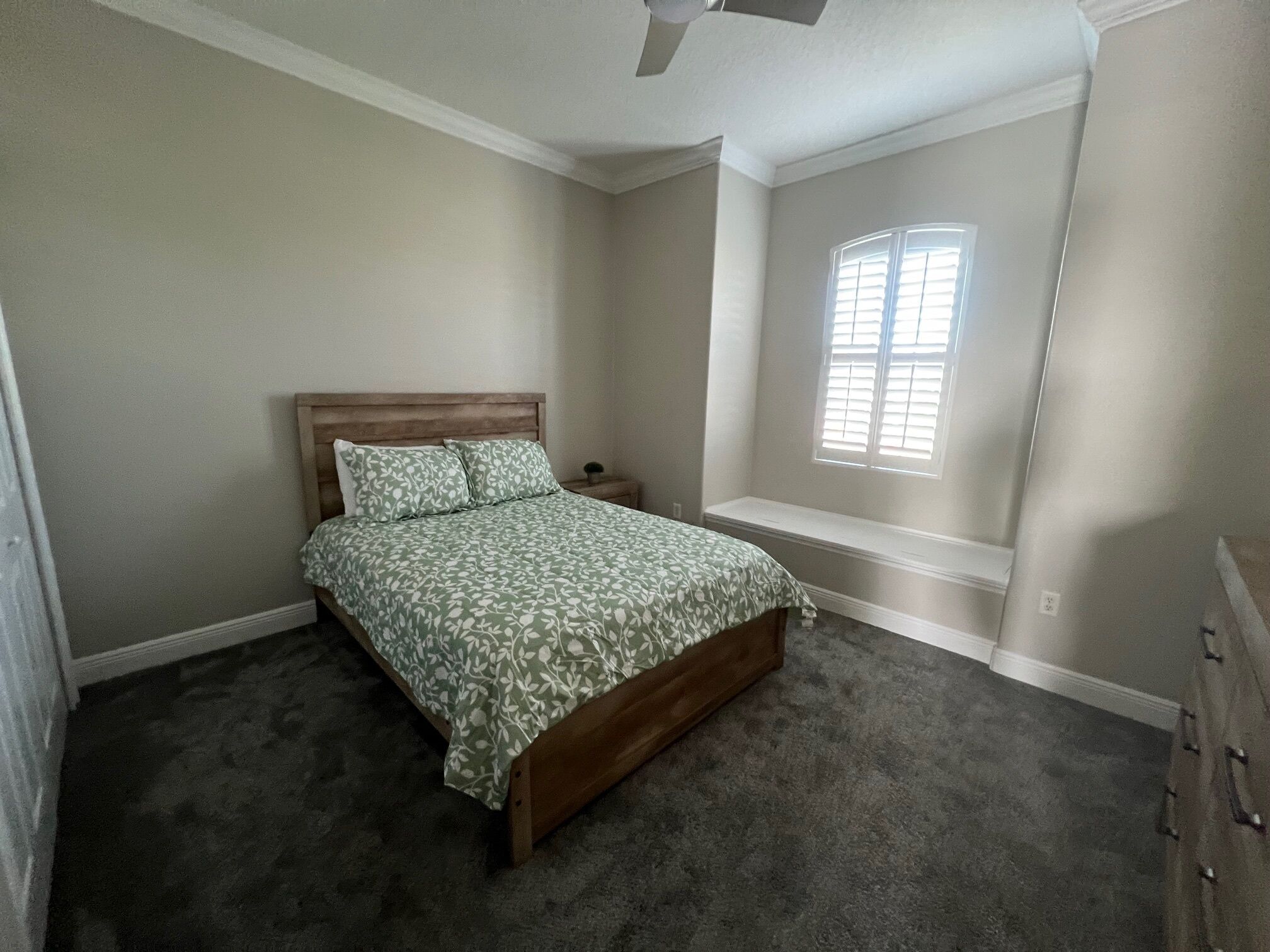 A bedroom with a bed, a nightstand, a window with blinds, and a ceiling fan.